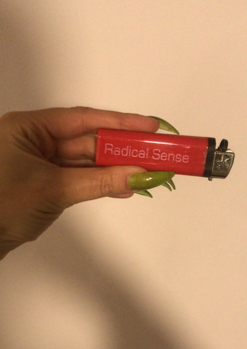 A photograph of a thumb and forefinger, with long, varnished transparent lime green nails, holding a red lighter inscribed with the words “Radical Sense” in pink Eurostile type.